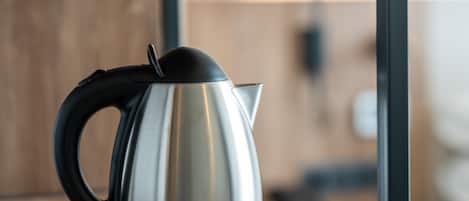 A stainless steel kettle with a black handle and lid on a wooden surface.