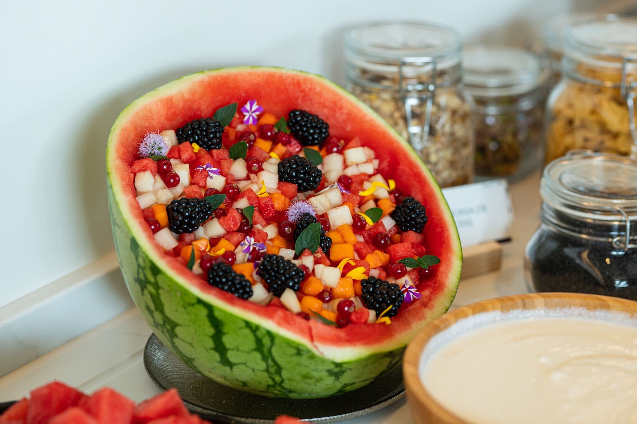 Una ciotola di insalata di frutta servita in una ciotola di anguria, con diversi tipi di frutta e erbe aromatiche.