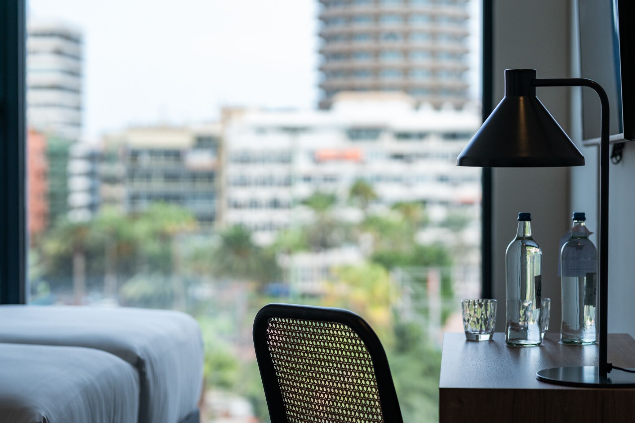 Une chambre d’hôtel avec un lit, une chaise, un bureau avec une lampe et des bouteilles.