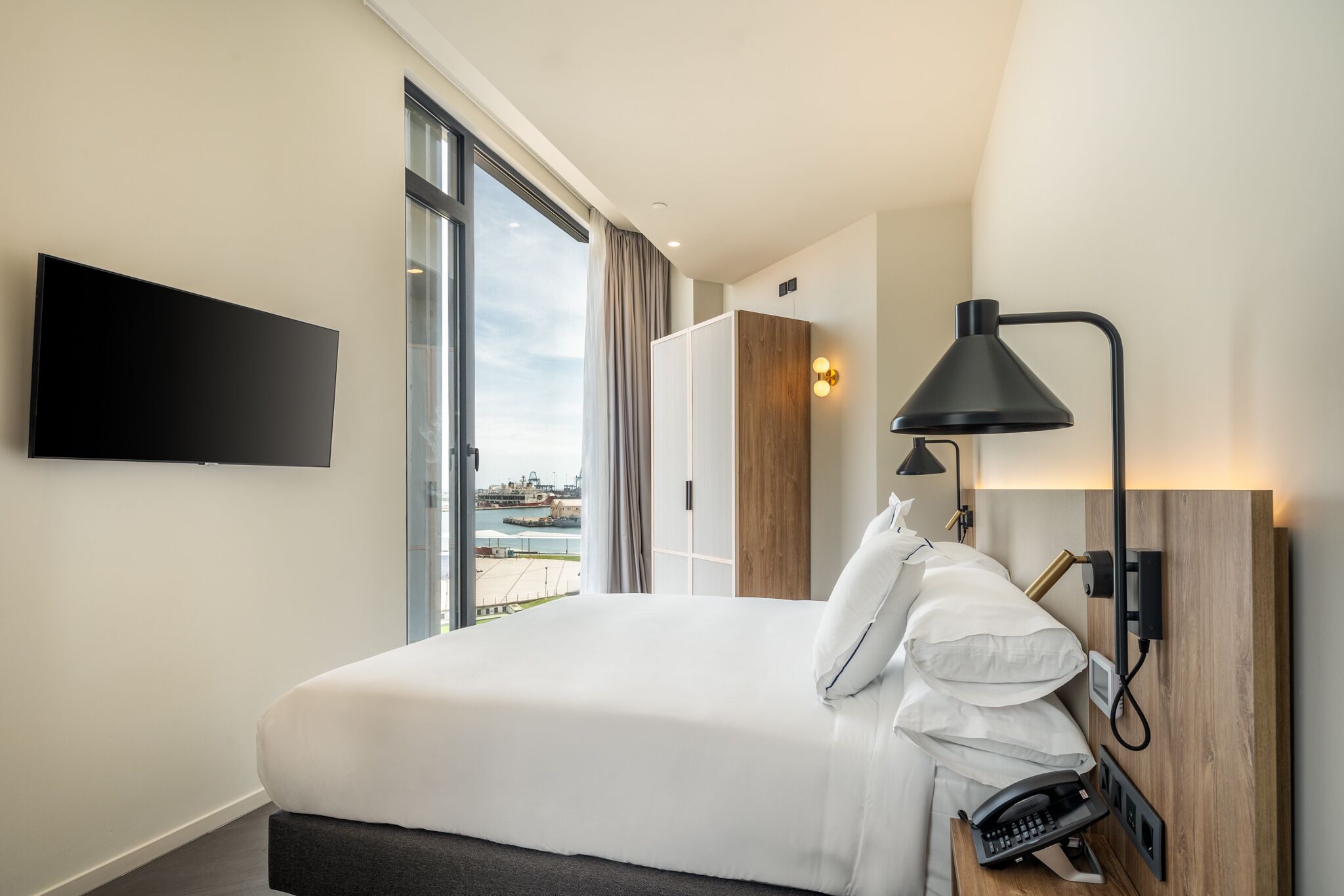 Une chambre d’hôtel avec un lit, une télévision, un bureau avec un téléphone, une lampe et une vue sur une étendue d’eau.