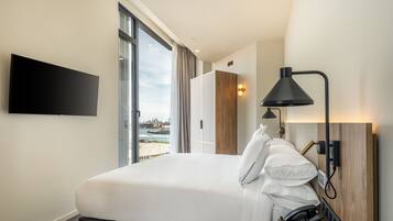 Une chambre d’hôtel avec un lit, une télévision, un bureau avec un téléphone, une lampe et une vue sur une étendue d’eau.