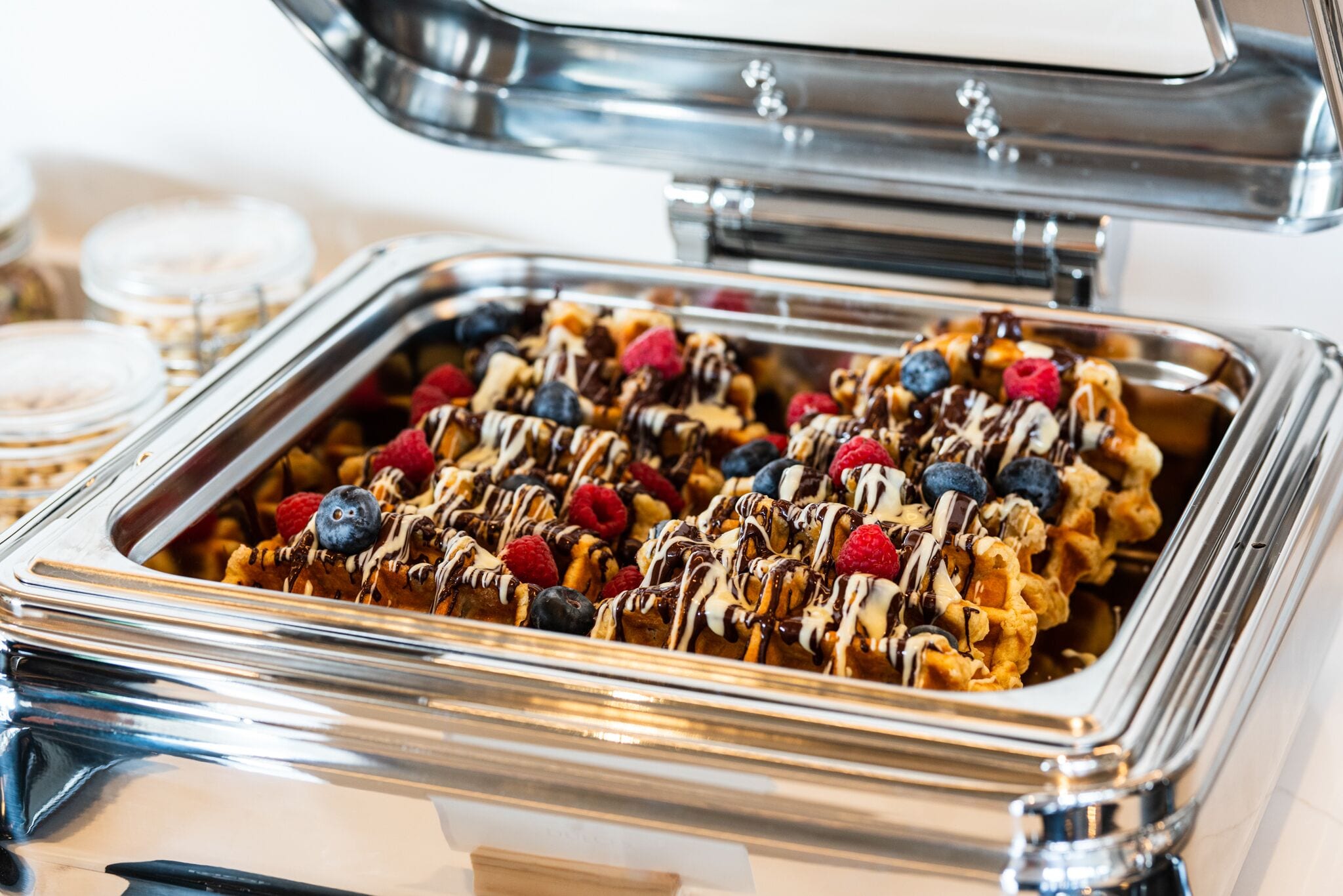 Un bufé con waffles cubiertos de frutos rojos y salsa de chocolate.