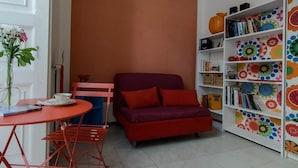 A cozy room with a red sofa, a small table with a cup, and a bookshelf with colorful patterns. - In the heart of Naples (Napoli)