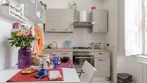 A kitchen with white cabinets, a stove, and a sink. There is a table with a vase of flowers and a plate of food. - In the heart of Naples (Napoli)