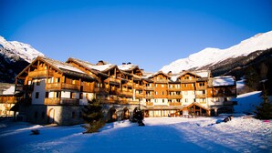 A large wooden hotel with multiple balconies and a snow-covered mountain backdrop. - travelski home premium - Résidence Les Alpages de Val Cenis 4* - 3 pièces 6 personnes (Lanslebourg-Mont-Cenis)