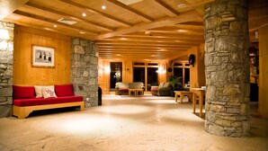 A spacious lobby with a wooden ceiling, stone pillars, a red sofa, and a stone fireplace. - travelski home premium - Résidence Les Alpages de Val Cenis 4* - 3 pièces 6 personnes (Lanslebourg-Mont-Cenis)