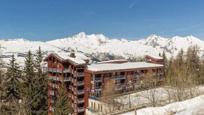 Un hotel de diverses plantes amb balcons, envoltat de muntanyes i arbres coberts de neu.
