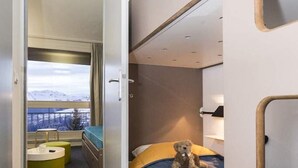 Una cabana moderna i compacta amb un llit superposat, una petita zona d'estar amb taula, i una finestra que ofereix una vista panoràmica.