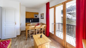 Una habitación compacta con una mesa de comedor, sillas, una pequeña cocina y un ventanal corredero que da a un balcón.