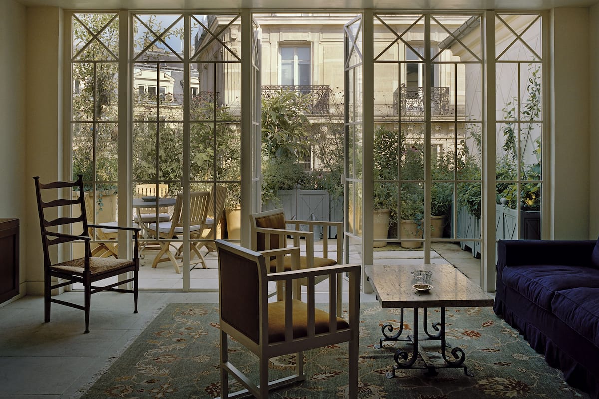 A sunlit room with large windows, a wooden table, two chairs, and a purple sofa.