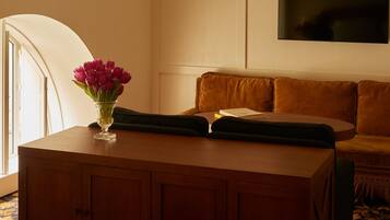 A room with a wooden cabinet, a vase of flowers, a sofa, and a flat-screen TV on the wall.