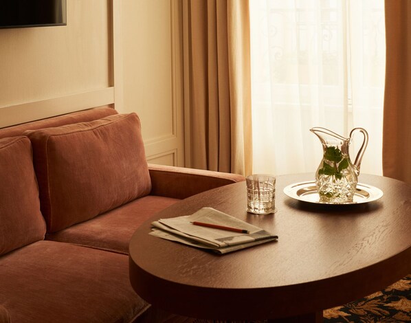 A cozy room with a brown sofa, a round wooden table, a glass pitcher with a plant, and a glass of water.