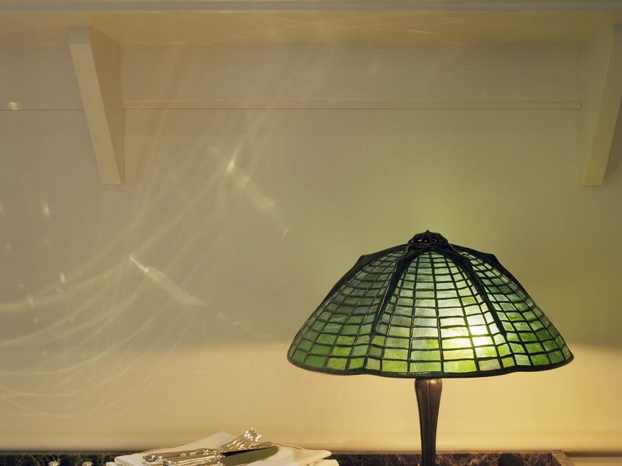 Un piano di lavoro in cucina con una lampada a mosaico verde, piatti impilati e una ciotola decorativa.