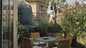 An outdoor patio with a round table and four wooden chairs, surrounded by lush greenery and a view of a residential building. - Hôtel Château Voltaire (Paris)