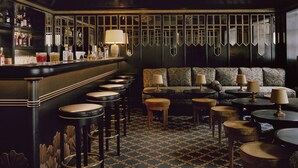 A bar area with stools, a bar counter, and a seating area with patterned sofas and tables. - Hôtel Château Voltaire (Paris)