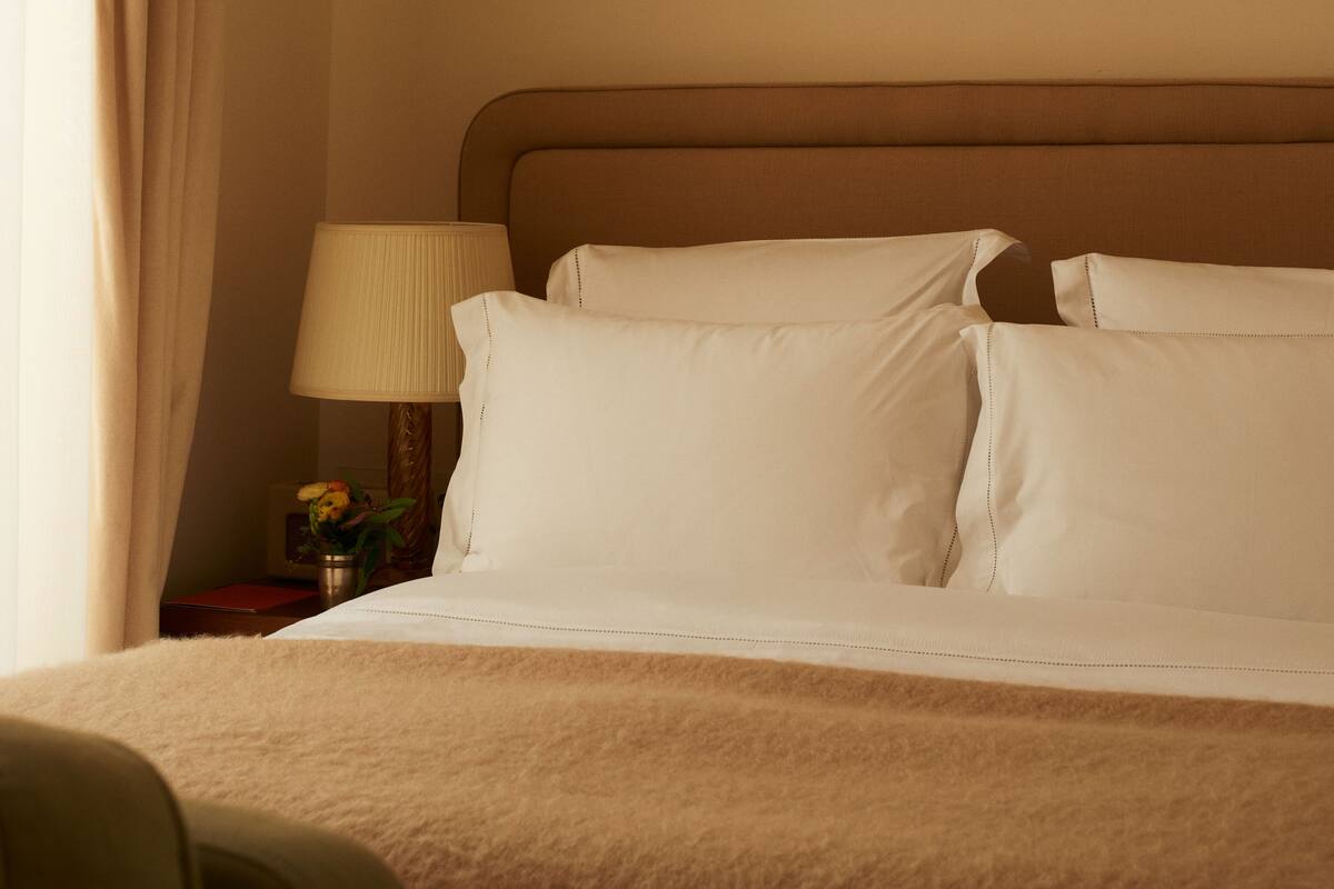 A neatly made bed with white linens, a bedside lamp, and a framed abstract painting on the wall.