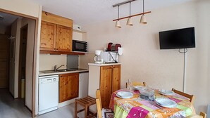 A compact kitchen with wooden cabinets, a microwave, and a coffee maker. There is a dining table set with plates and glasses. - travelski home classic - Résidence Boedette - Studio 4 personnes 515 (Les Menuires)
