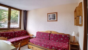A cozy room with a wooden bench and a sofa, a small table, and a window with a view of trees. - travelski home classic - Résidence Boedette - Studio 4 personnes 515 (Les Menuires)