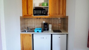 Eine kompakte Küche mit Holzausstattung, einer Mikrowelle, einer Kaffeemaschine und einem Geschirrspüler.