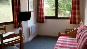 Ein Schlafzimmer mit Bett, Sessel, Fernseher und einem Fenster mit Vorhängen.