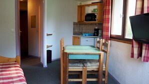 Ein gemütlicher Raum mit einem Bett, einem Holztisch mit Stühlen, einer Küchenzeile mit einer Mikrowelle und einem Fernseher an der Wand.
