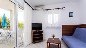 Een kamer met een televisie, een bank, een tafeltje en een balkon met een tafel en stoelen.