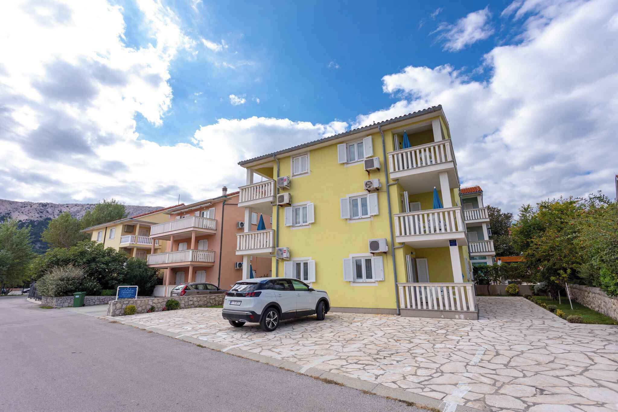 A multi-story residential building with balconies, a stone-paved driveway, and a parked car.