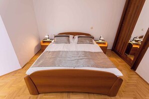 Una cama bien hecha con cabecera de madera, dos mesitas de noche con lámparas y un espejo en la pared.
