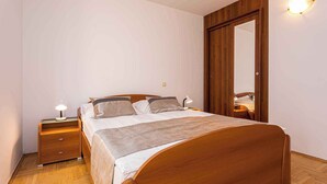Un dormitorio con cama de madera, dos mesitas de noche con lámparas, un armario y un espejo.