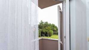 Varanda com tela branca e porta que dá para um jardim com árvores e arbustos.
