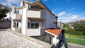 Um edifício residencial de vários andares com varandas, um pátio com piso de pedra e montanhas ao fundo.