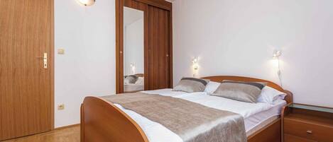 A bedroom with a wooden bed, a nightstand, a mirror, and two wall-mounted lights.