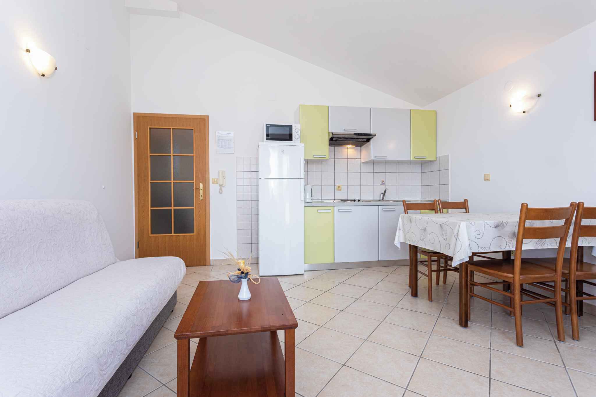 A compact living space with a kitchenette, a sofa, a dining table with chairs, and a small decorative vase.