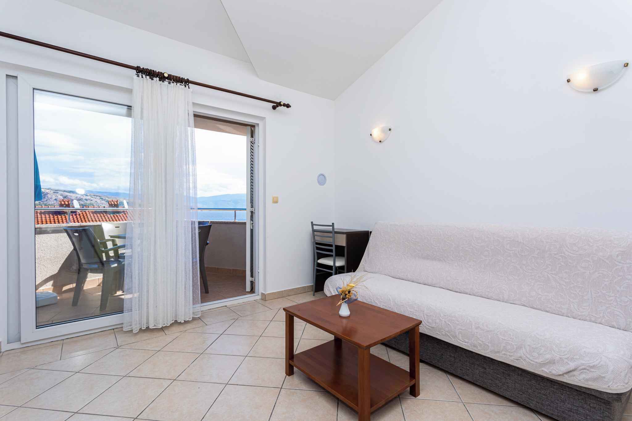 Ein Wohnzimmer mit einer Couch, einem kleinen Holztisch und Blick durch eine Schiebetür auf einen Außenbereich mit Tisch und Stühlen.