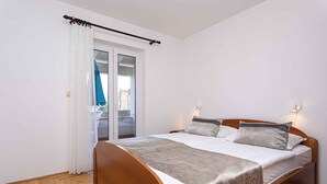 A bedroom with a wooden bed, white curtains, and a view of a balcony. - Holiday apartment by the sea with barbecue and panoramic view (Baška)