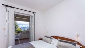 A bedroom with a bed, a nightstand, a wall-mounted light, and a balcony with a view of the city. - Holiday apartment by the sea with barbecue and panoramic view (Baška)