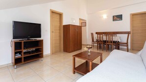 A modern living room with a flat-screen TV, wooden furniture, a dining area, and a large bed. - Holiday apartment only 100 m from the sea (Baška)