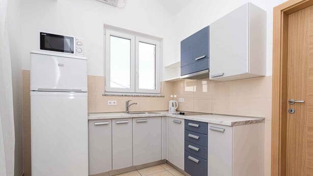 A compact kitchen with a refrigerator, microwave, sink, and cabinets. - Holiday apartment only 100 m from the sea (Baška)
