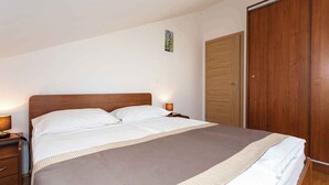 A bedroom with a wooden bed, a nightstand, a bedside lamp, and a wardrobe. - Holiday apartment only 100 m from the sea (Baška)