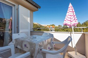 Ein Balkon mit Tisch und Stühlen, einem gestreiften Sonnenschirm und Blick auf einen Berg und ein Haus.