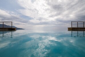 Vista deslumbrante de uma piscina infinita com guarda-corpo metálico de um lado e montanha ao fundo.