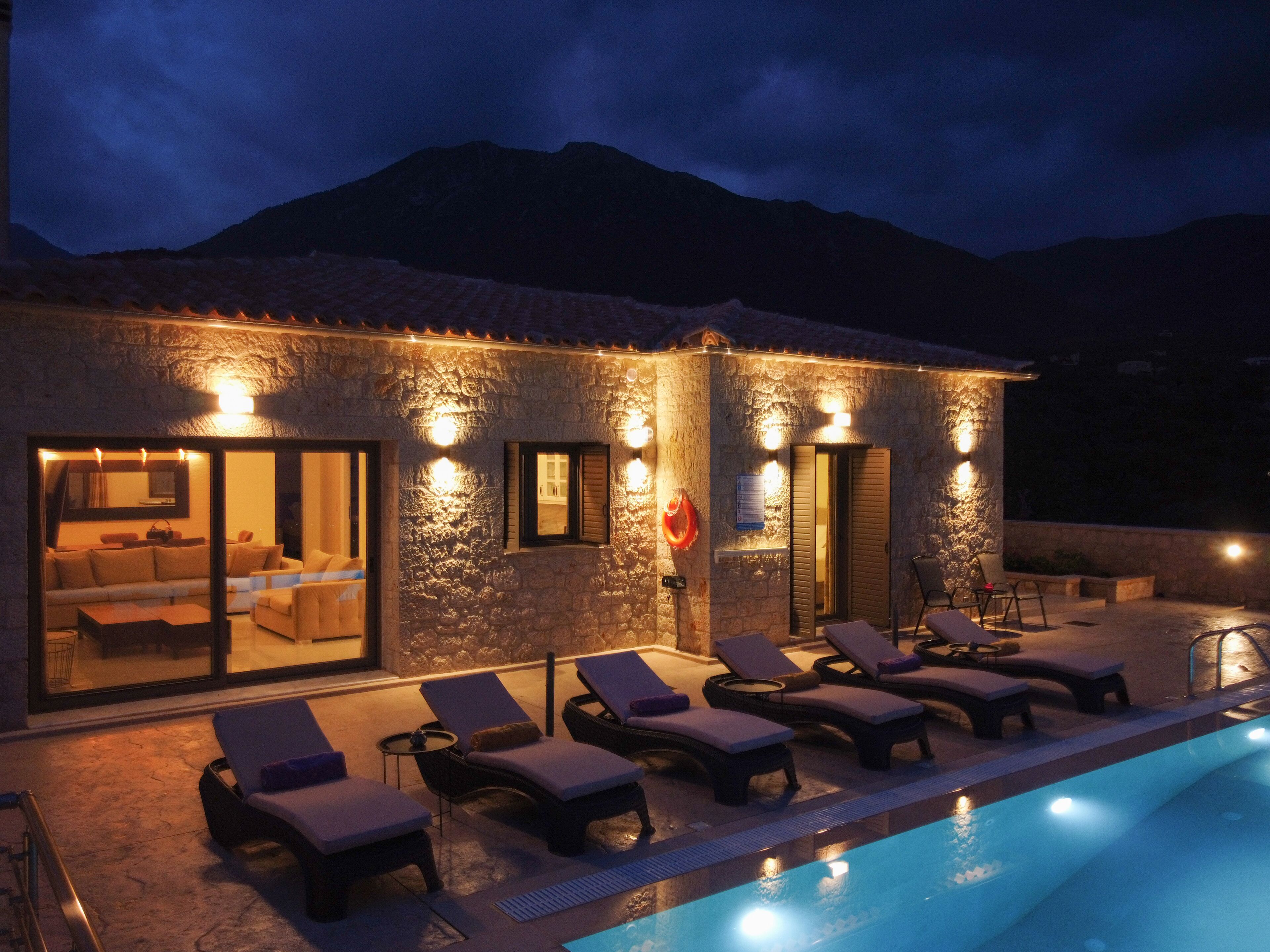 A stone building with a swimming pool, lounge chairs, and a view of mountains.