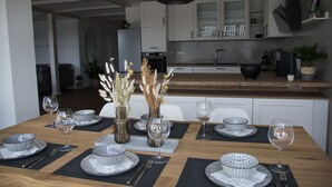 Zona de menjador amb taula de fusta preparada per a sis, amb plats de disseny blanc i negre i copes de vi transparent.