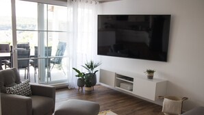Un saló modern amb televisió de pantalla plana penjada a la paret, un sofà, una taula de centre i una zona menjador amb caires i taula.
