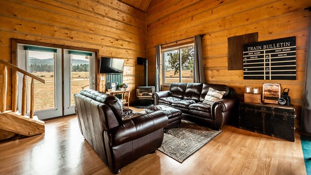 A wooden cabin interior with a leather sofa, a mounted TV, and a train bulletin board. - Railroad Baron (Superior)