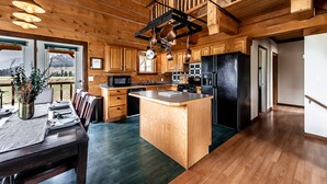 A spacious kitchen with wooden cabinets, a central island, and a dining area with a view of mountains. - Railroad Baron (Superior)