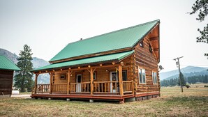A log cabin with a green roof, wooden porch, and a mountainous backdrop. - Railroad Baron (Superior)