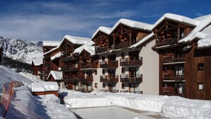 Una stazione sciistica innevata con edifici in legno, balconi e una seggiovia sullo sfondo.