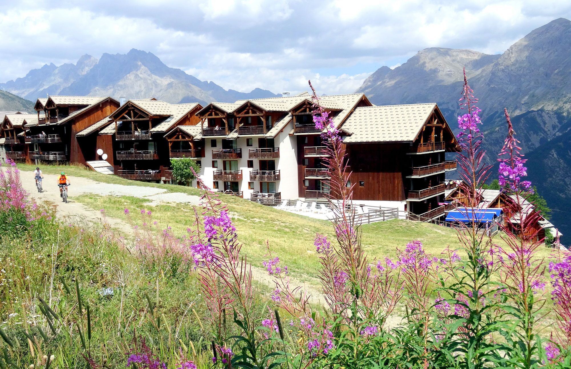 A row of wooden chalets with balconies, set against a mountainous backdrop.