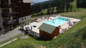 Zona piscina con lettini e un piccolo edificio in legno, immersa in un paesaggio montuoso.